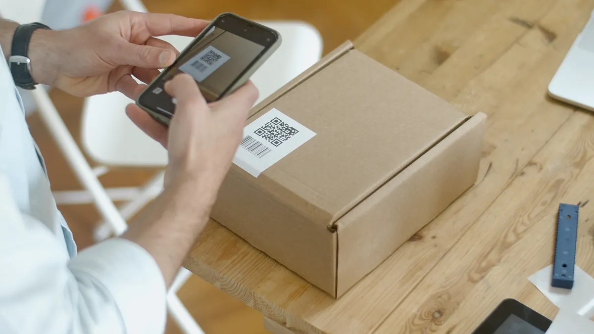 Hands scanning a labeled shipping box with a smartphone