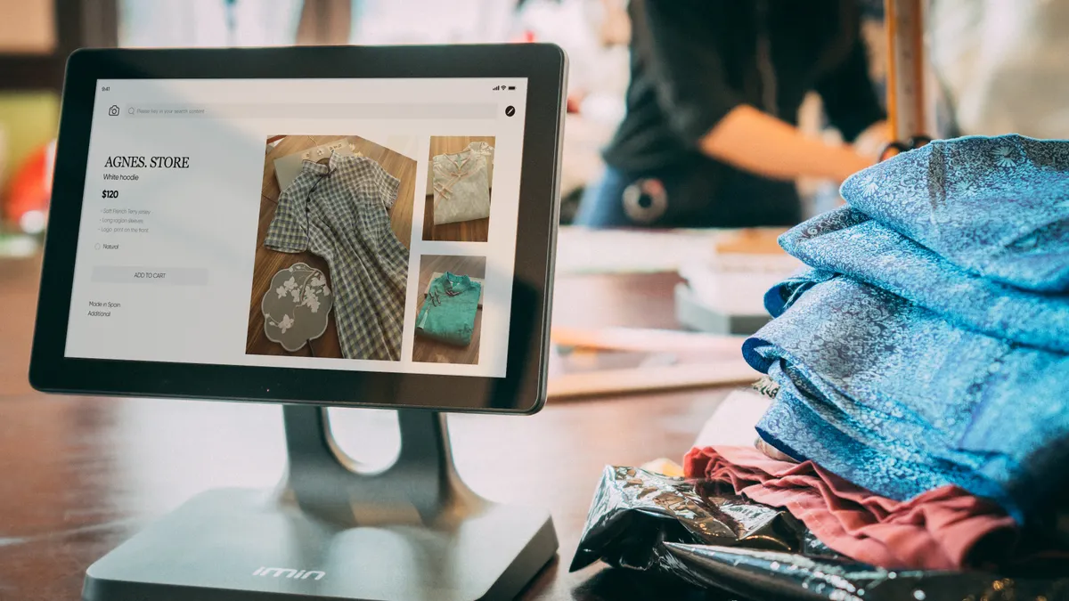 Retail product page on a touchscreen beside folded clothes